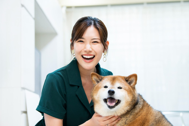 オフィスホワイトニングをした白い歯の女性が笑顔で愛犬を可愛がるイメージ