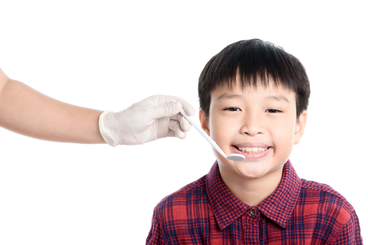 子どもに歯科検診をするデンタルミラーを持った歯科医の手