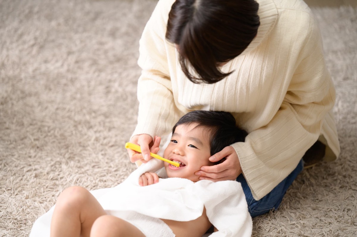 母親の膝に頭をのせて仕上げ磨きをしてもらう子ども